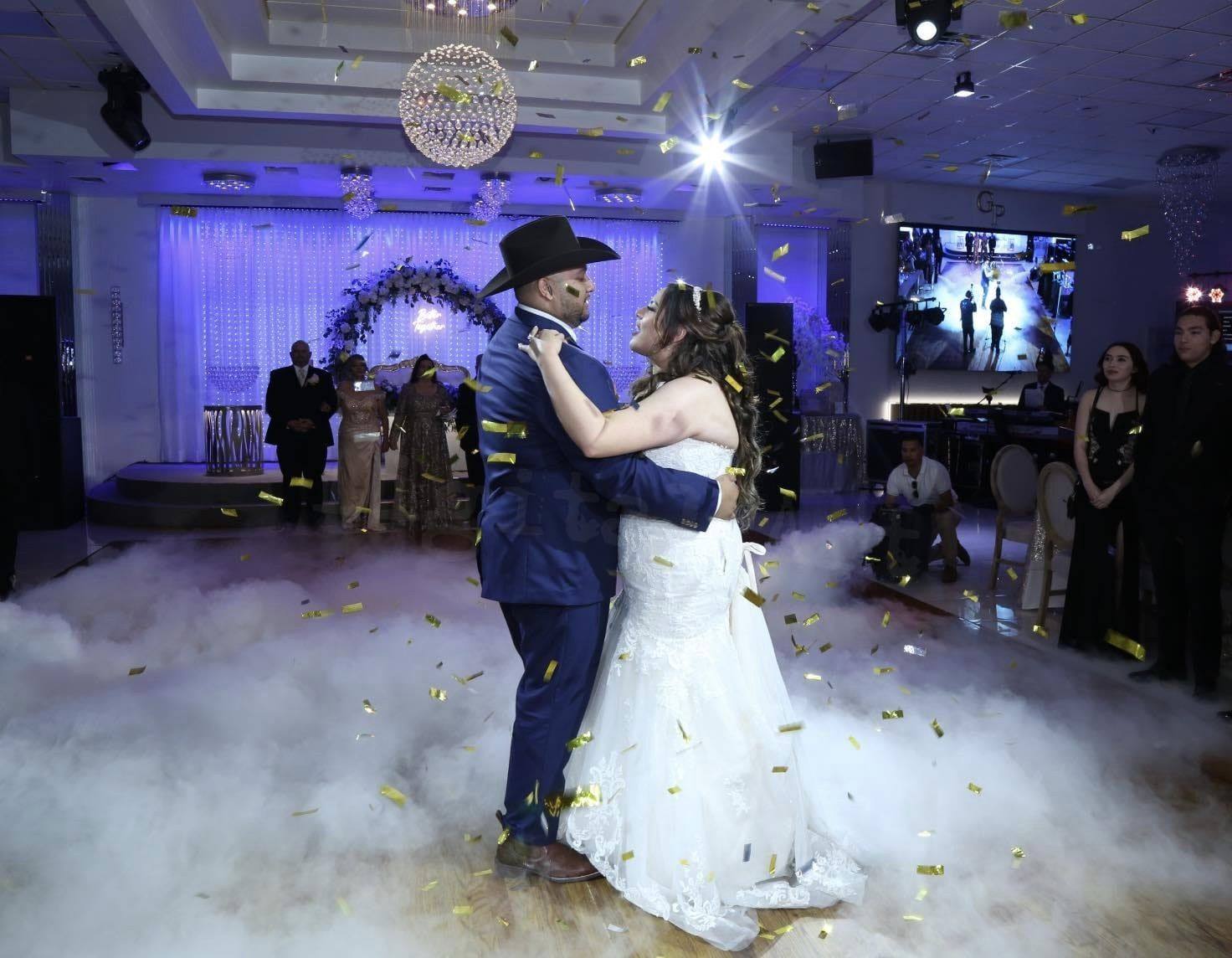 A wedding head table on a draped stage with an illuminated LOVE sign and crystal chandeliers
