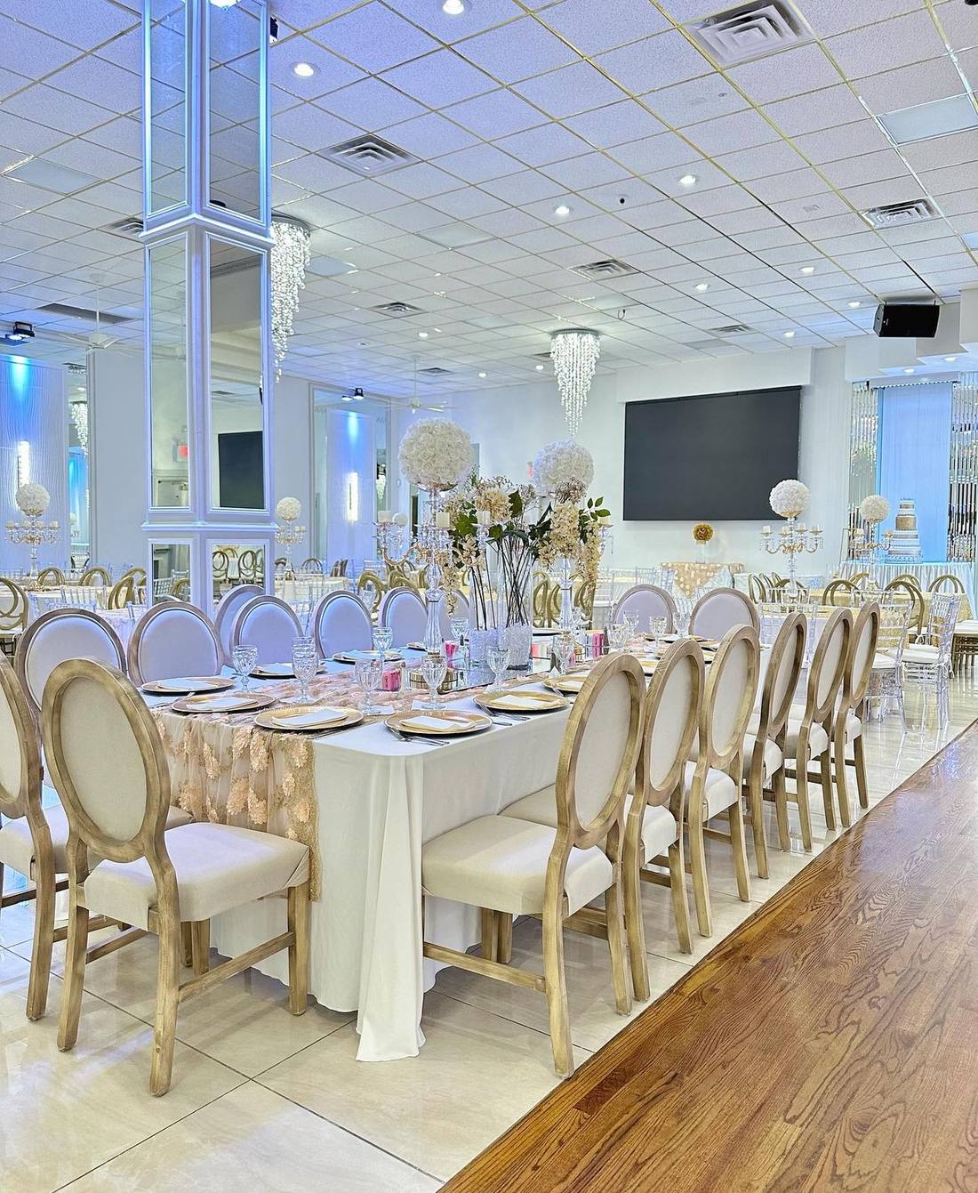 A long banquet table set with gold chargers and floral centerpieces inside The Grand Palace Ballroom