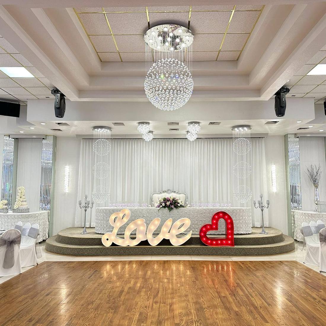 The ballroom stage dressed in white with an illuminated LOVE sign and crystal chandeliers
